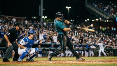Baseball players in a tense MLB matchup under stadium lights as a batter connects with a pitch.